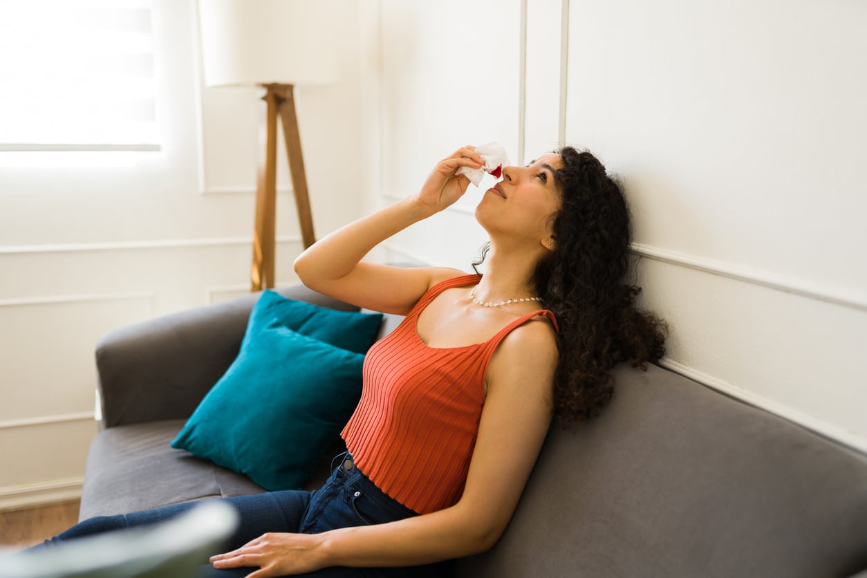 Woman suffering from nosebleed at home.