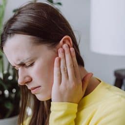 Woman holding her ear, suffering from tinnitus.