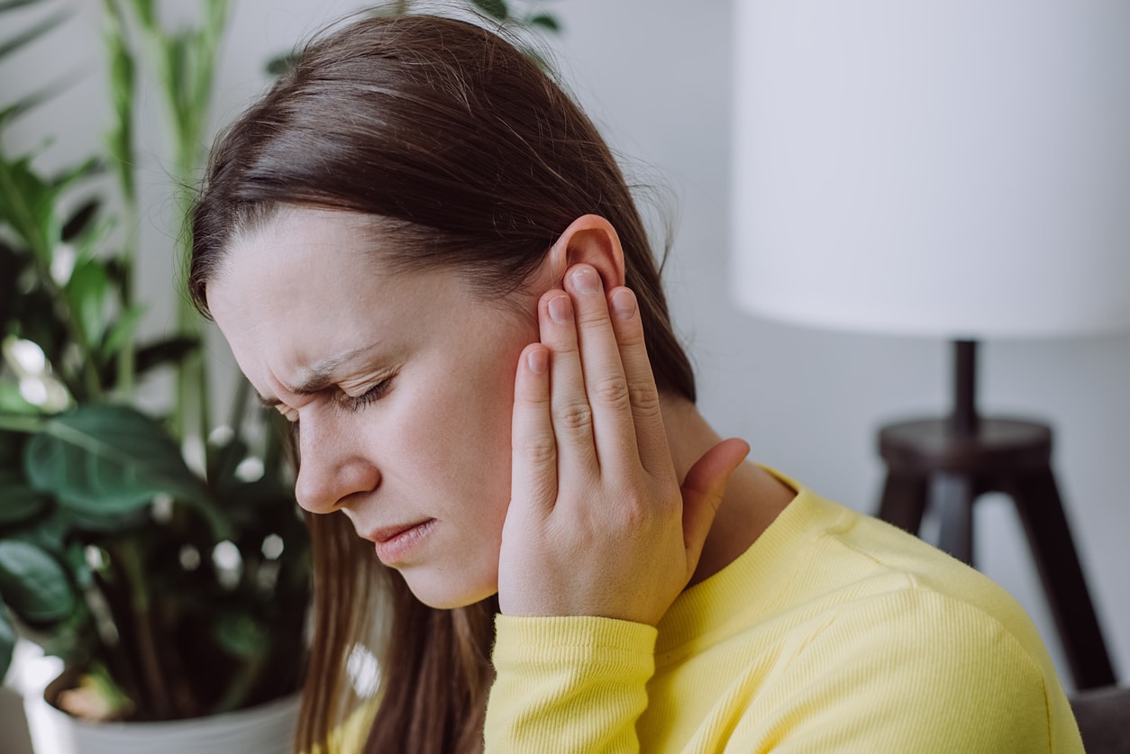 Woman holding her ear, suffering from tinnitus.