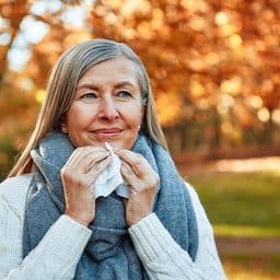 Smiling woman holding a tissue while standing in a park in autumn.