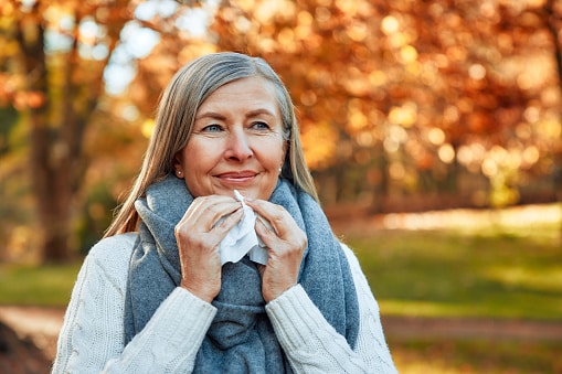 Smiling woman holding a tissue while standing in a park in autumn.