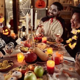 Happy family in costumes talking while having a Halloween meal at their dining table.
