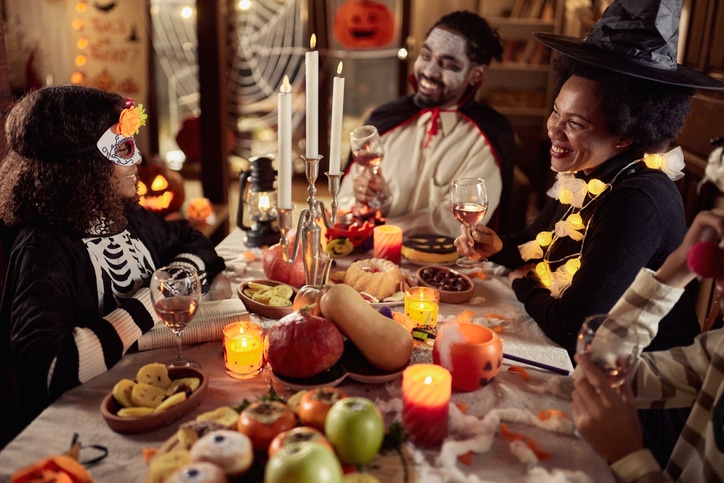 Happy family in costumes talking while having a Halloween meal at their dining table.